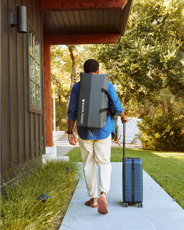 A man walking and carrying the Lotus Travel Crib in its carrying case